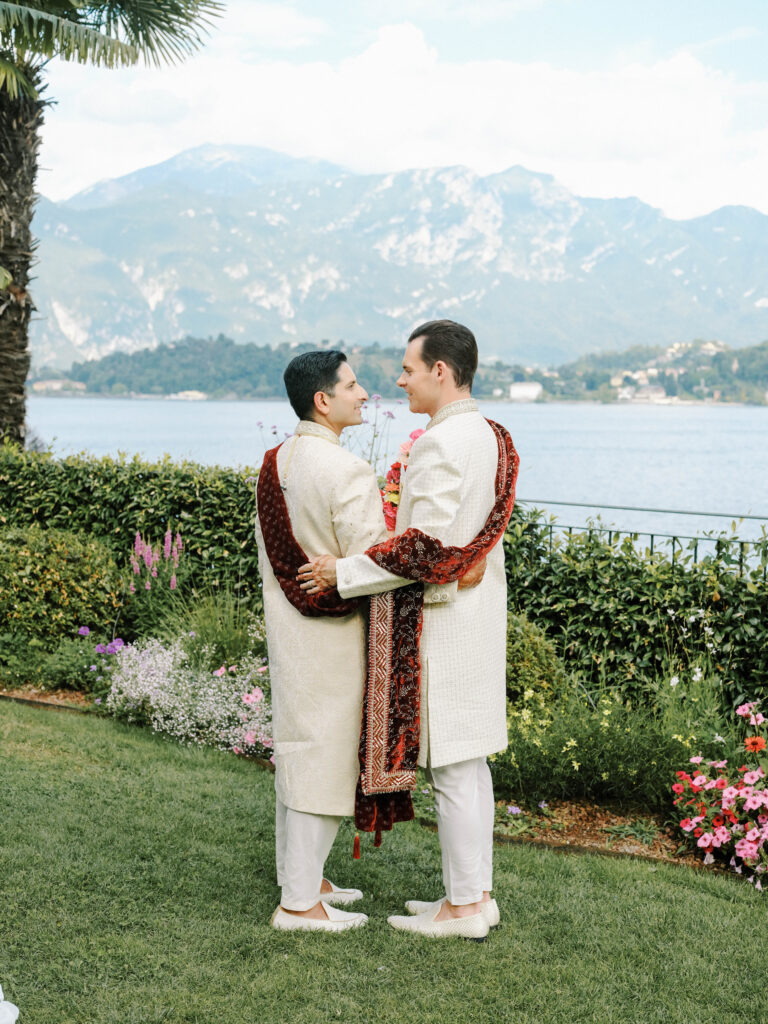 same sex and multi-faith couple in Indian sherwanis hugging by Lake Como