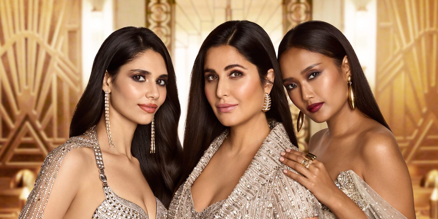 Katrina Kaif with two models wearing Kay Beauty x Falguni Shane Peacock makeup, showcasing glowing skin, matte lip colours, and sleek hair against a gold Art Deco backdrop.