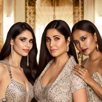 Katrina Kaif with two models wearing Kay Beauty x Falguni Shane Peacock makeup, showcasing glowing skin, matte lip colours, and sleek hair against a gold Art Deco backdrop.